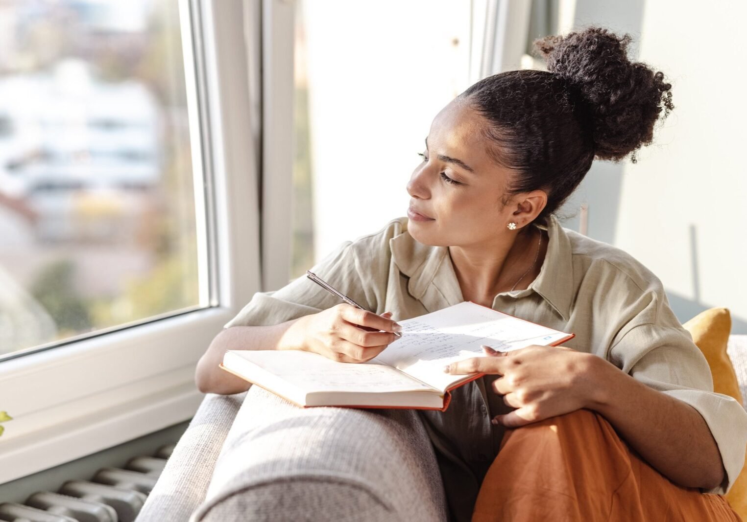 A young woman is at home, she is sitting on the sofa in the living room and writing notes