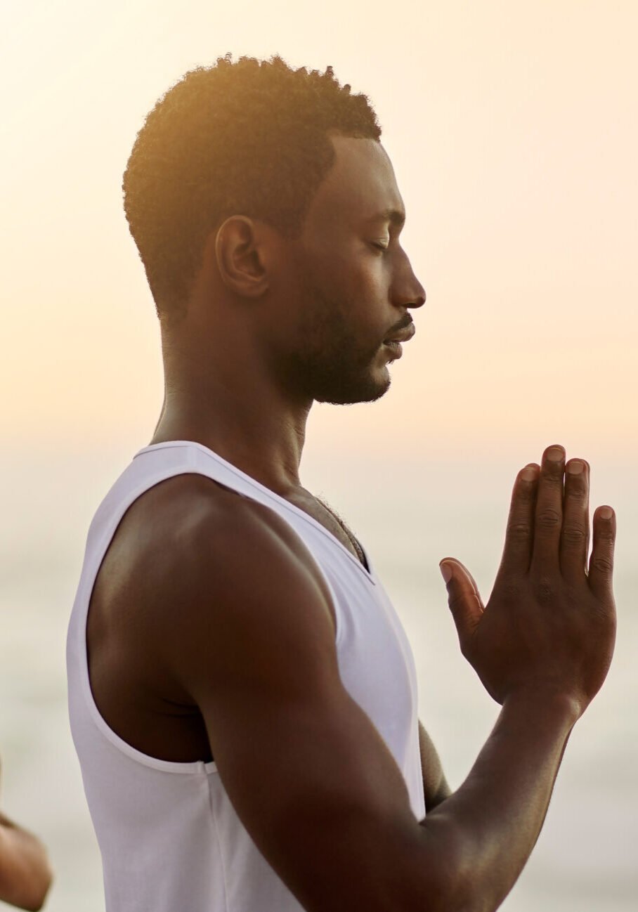 Relaxed, healthy and zen couple meditating on a beach in namaste prayer hands pose by sea and ocean. Calm and spiritual yogis breathing, worshipping and showing thanks in holistic mental health yoga