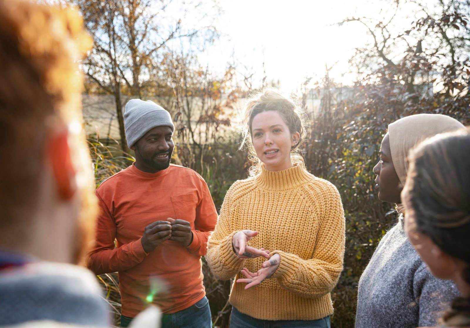 A multiracial group of volunteers wearing warm casual clothing and accessories on a sunny cold winters day. They are talking before they start working on a community farm, planting trees and performing other tasks.